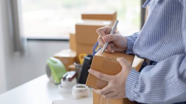 Genç Asyalı kadın, müşterinin bilgilerini ve adreslerini posta kutusuna yazıp bilgilere göre nakliyeye hazırlanıyor..