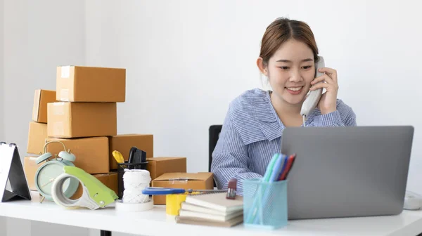 Asian businesswoman is taking online orders from a phone and chatting with customers to confirm their order, Selling products online or doing freelance work at home concept.