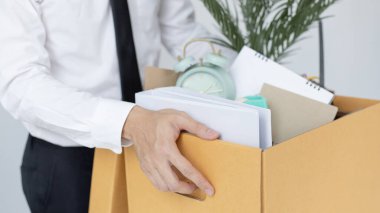 Siyah takım elbiseli bir işadamı ofisten kahverengi bir karton kutu kaldırıyor, iş adamları istifa veya işten çıkarıldıktan sonra kişisel eşyalarını ve ekipmanlarını topluyor, iş sözleşmesinin süresi doluyor..