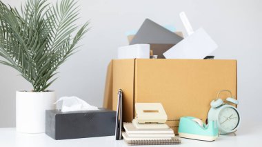 Brown cardboard box inside contains office equipment and resignation envelopes, Relocating or changing jobs or getting promoted, Resignation letter. clipart