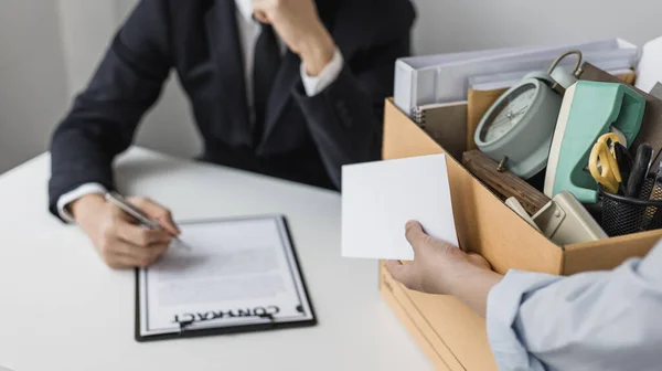 Employee handed over a document envelope and a box of work equipment beside him, Woman submits resignation documents to their supervisor and take personal equipment in a brown box from the office.