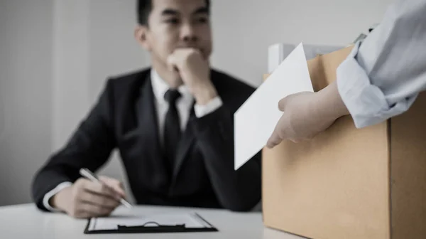 Employee handed over a document envelope and a box of work equipment beside him, Woman submits resignation documents to their supervisor and take personal equipment in a brown box from the office.