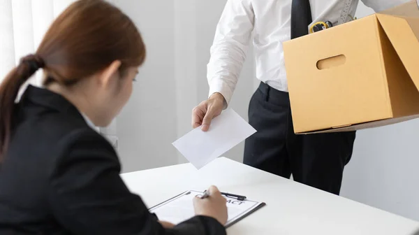 Employee handed over a document envelope and a box of work equipment beside him, Businessman submits resignation documents to their supervisor and take personal equipment in a brown box from the office.
