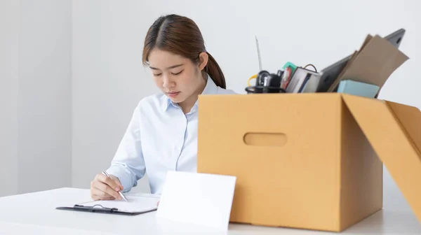 Businesswoman in a blue shirt sat filling out the letter of resignation and there was a box of personal work equipment next to it, Prepare to move to a new place of work or be laid off, been dismissed