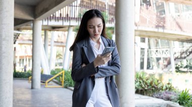 Gri takım elbiseli genç kadın akıllı telefon üzerinde çalışırken gergin görünüyor, iş kadını işten dolayı stresli çünkü akıllı telefondan gönderilen veriler yanlış, endişeli, üzgün, yanlış, depresyonda..