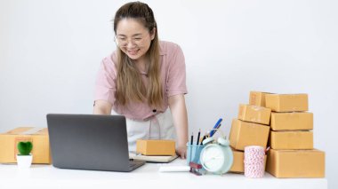 Genç bir kadın, sipariş vermeye gelen müşterilerle sohbet etmek için dizüstü bilgisayar kullanıyor. Evden çalışabilen ve mallarını postayla teslim edebilen yeni genç işletmeler, internette veya internette satış yapabilen şirketler..