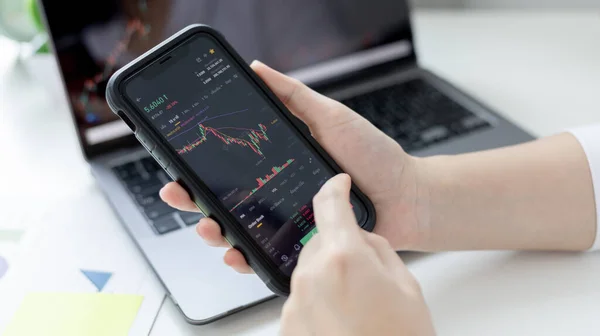 Genç bir iş kadınının elinde borsa verilerinin grafiği olan bir telefon var ve borsa kazanımını ve zararını analiz ediyor. Borsa verilerinin analizi için bu anlaşmayı yapın..