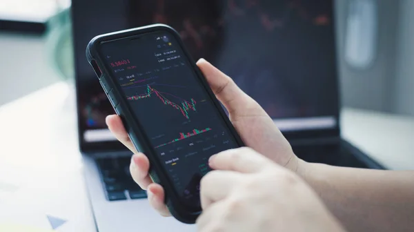 Hand of a young business woman holds a phone with a graph of the stock market data and analyzes the stock market gain and loss, do this deal on a stock exchange, Analysis of stock market data.