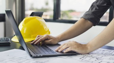 Dizüstü bilgisayarı olan genç bir adam planlarda, mimarlarda ya da mühendislerde yapılar inşa eden bir sistem çiziyor. Fiziksel yapıyı doğru hesaplamak için bilgisayar kullanıyorlar..