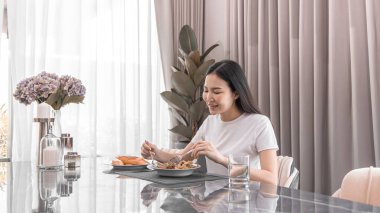 Yemek masasında salata yiyen Asyalı kadın gülümsüyor ve mutlu, sebze salataları vitamin ve mineraller, düşük kalorili ve yüksek lifli diyetler, taze sebze yiyerek sağlık hizmetleri açısından zengindir..