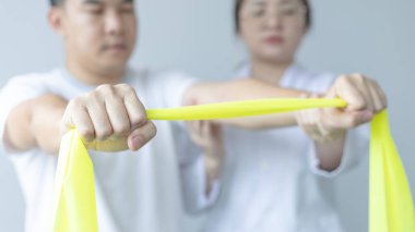 Fizyoterapi, kadın fizyoterapist, kliniğe giden bir erkeğin kol yaralanmasını, kemik düzenini, cerrahi olmayan tıbbi tedaviyi ve tıbbi teknikleri test etmek için elastik bant kullanıyor..