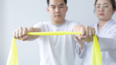 Fizyoterapi, kadın fizyoterapist, kliniğe giden bir erkeğin kol yaralanmasını, kemik düzenini, cerrahi olmayan tıbbi tedaviyi ve tıbbi teknikleri test etmek için elastik bant kullanıyor..