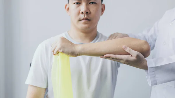 物理治疗中 女性理疗师使用弹性带检测在诊所就诊的男性患者的手臂损伤 骨排列 非手术治疗 医疗技术 — 图库照片
