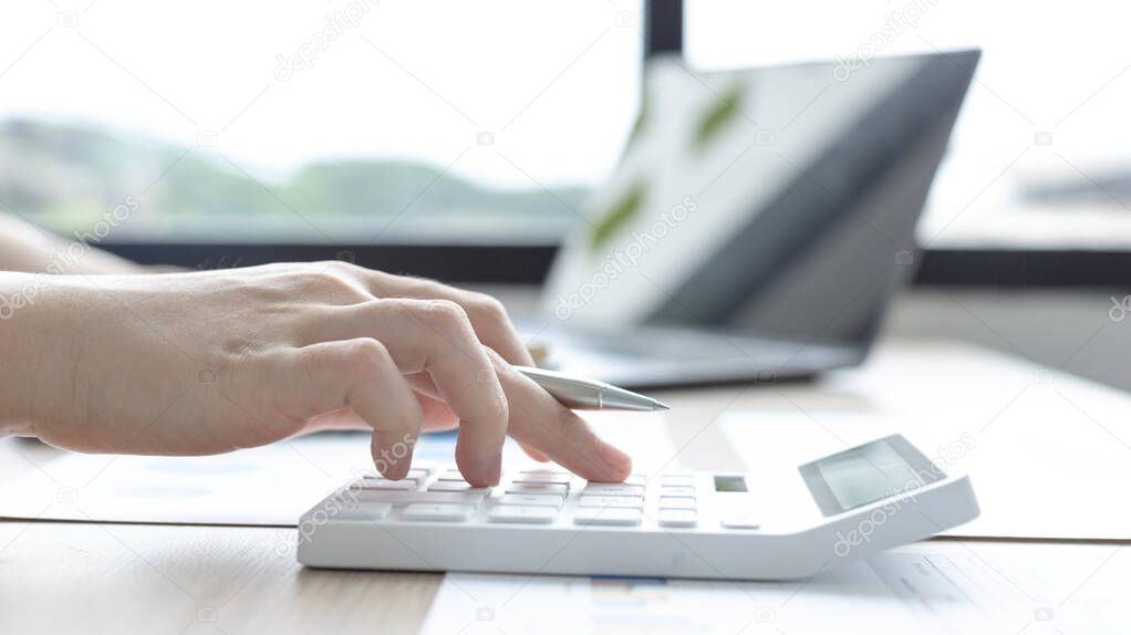 Young Asian businesswoman presses a calculator to calculate income tax and corporate income in a private office, Finance, Accounting, Tex, Statistical graphs of marketers investing in real estate.