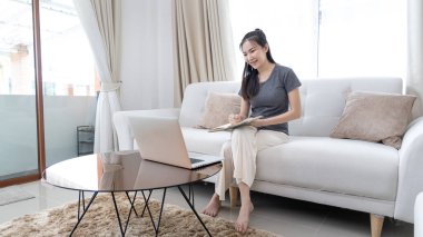 Not defterine not alan Asyalı kadın evde dizüstü bilgisayar, görüntülü sohbet, online iletişim, Evde kal, Yeni Normal, Covid-19 Coronavirus, Sosyal Mesafe, Çevrimiçi Öğren.