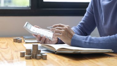 Adam yıl boyunca biriktirdiği parayı hesaplamak için hesap makinesine basıyor, gelecek için para biriktiriyor, madeni paralar masanın üstüne yığılıyor. İş yatırımı, Finans ve Muhasebe.