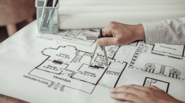 Genç adamın yapısal tasarımı ya da mühendisi bir kat planı ya da planı etrafında bir ölçüm çemberi kullanıyor, mimar ya da mühendis fiziksel yapıyı çizmek için pusula kullanıyor.