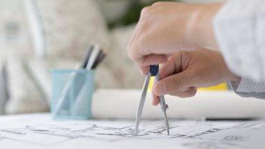 Genç adamın yapısal tasarımı ya da mühendisi bir kat planı ya da planı etrafında bir ölçüm çemberi kullanıyor, mimar ya da mühendis fiziksel yapıyı çizmek için pusula kullanıyor.