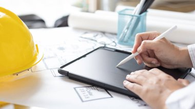 Tablet kullanan genç adam, planlarda, mimarlarda veya mühendislerde yapı inşa etme sistemi çizerek, fiziksel yapıyı doğru hesaplamak için tablet kullanarak binalar tasarlıyor..