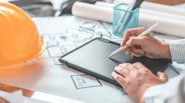 Tablet kullanan genç adam, planlarda, mimarlarda veya mühendislerde yapı inşa etme sistemi çizerek, fiziksel yapıyı doğru hesaplamak için tablet kullanarak binalar tasarlıyor..