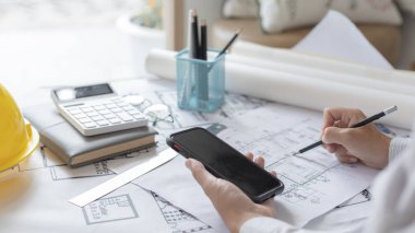 Smartphone 'u kullanan genç adam planlarda, mimarlarda ya da mühendislerde yapı yapıları oluşturan bir sistem çiziyor. Binaları, fiziksel yapıyı doğru hesaplamak için cep telefonu kullanarak tasarlıyorlar..