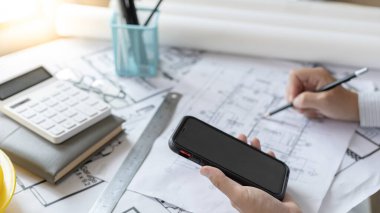 Smartphone 'u kullanan genç adam planlarda, mimarlarda ya da mühendislerde yapı yapıları oluşturan bir sistem çiziyor. Binaları, fiziksel yapıyı doğru hesaplamak için cep telefonu kullanarak tasarlıyorlar..