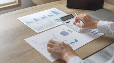 Genç Asyalı işadamı gelir vergisi ve kurumsal geliri hesaplamak için özel bir ofis, Finans, Muhasebe, Tex ve emlak yatırımlarına yatırım yapan pazarlamacıların istatistiksel grafiklerini hesaplamak için hesap makinesine baskı yapıyor.