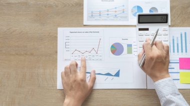 Genç Asyalı işadamı gelir vergisi ve kurumsal geliri hesaplamak için özel bir ofis, Finans, Muhasebe, Tex ve emlak yatırımlarına yatırım yapan pazarlamacıların istatistiksel grafiklerini hesaplamak için hesap makinesine baskı yapıyor.