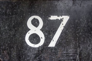 Taş bir duvarda seksen yedi (87) numaralı ev boyanmış.