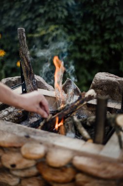 Yazlık evlerindeki ızgarada odundan yakılan şenlik ateşi. Ateşten gelen parlak alev. Bir adam şenlik ateşi yakıyor. Ellerini ateşin yanına koy.