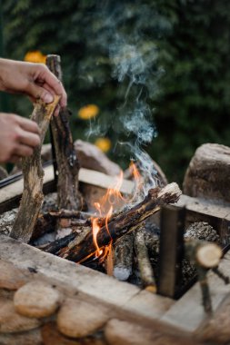 Yazlık evlerindeki ızgarada odundan yakılan şenlik ateşi. Ateşten gelen parlak alev. Bir adam şenlik ateşi yakıyor. Ellerini ateşin yanına koy.