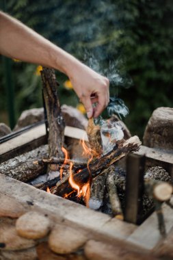 Yazlık evlerindeki ızgarada odundan yakılan şenlik ateşi. Ateşten gelen parlak alev. Bir adam şenlik ateşi yakıyor. Ellerini ateşin yanına koy.