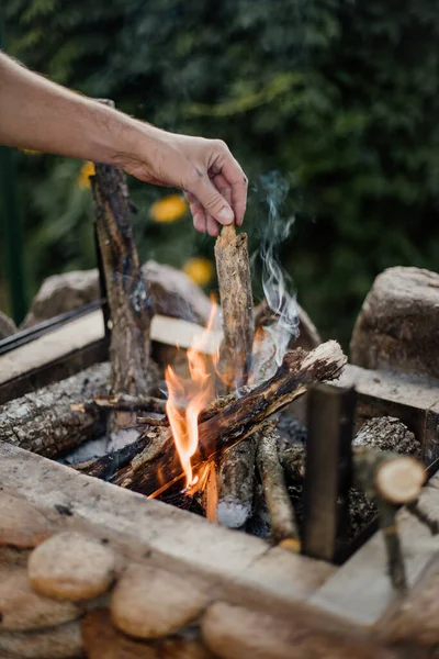 Bonfire lighted from wood in the grill at their summer cottage. Bright flame from the fire. A man lights a bonfire. Hands by the fire