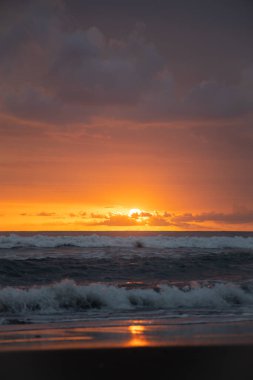 Bali 'de okyanusun kenarında inanılmaz güzel bir gün batımı. Parlak güneş suda batıyor. Güneş ışınları bulutların arkasından süzülüyor ve gün batımının suda güzel bir yansıması.