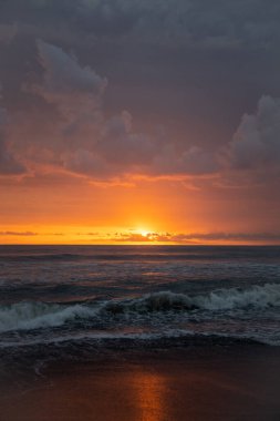 Bali 'de okyanusun kenarında inanılmaz güzel bir gün batımı. Parlak güneş suda batıyor. Güneş ışınları bulutların arkasından süzülüyor ve gün batımının suda güzel bir yansıması.
