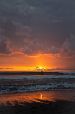 Bali 'de okyanusun kenarında inanılmaz güzel bir gün batımı. Parlak güneş suda batıyor. Güneş ışınları bulutların arkasından süzülüyor ve gün batımının suda güzel bir yansıması.