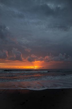 Bali 'de okyanusun kenarında inanılmaz güzel bir gün batımı. Parlak güneş suda batıyor. Güneş ışınları bulutların arkasından süzülüyor ve gün batımının suda güzel bir yansıması.
