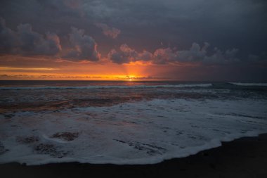 Bali 'de okyanusun kenarında inanılmaz güzel bir gün batımı. Parlak güneş suda batıyor. Güneş ışınları bulutların arkasından süzülüyor ve gün batımının suda güzel bir yansıması.