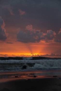 Bali 'de okyanusun kenarında inanılmaz güzel bir gün batımı. Parlak güneş suda batıyor. Güneş ışınları bulutların arkasından süzülüyor ve gün batımının suda güzel bir yansıması.