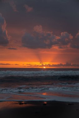 Bali 'de okyanusun kenarında inanılmaz güzel bir gün batımı. Parlak güneş suda batıyor. Güneş ışınları bulutların arkasından süzülüyor ve gün batımının suda güzel bir yansıması.