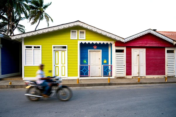 Непізнаний чоловік в русі на мотоциклі проходить колоритних дерев'яних будиночків в центр з Лас Терренас, Домініканська Республіка. — стокове фото
