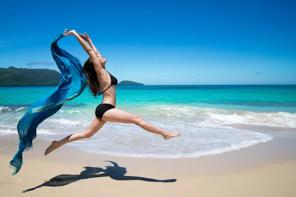Menina bonita pulando com capa azul ondulando, cachecol, na praia tropical no verão — Fotografia de Stock