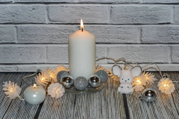 still life with a large white candle, electric lights in the form of cones, a white mouse and small silver Christmas balls in a glass round candlestick