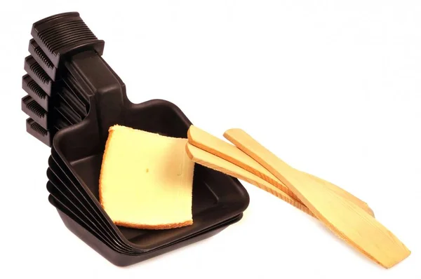 白い背景にチーズと木製のスパチュラのスライスが入ったラクレット料理 — ストック写真