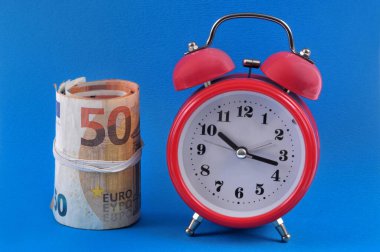 Mavi arka planda bir tomar avro banknotunun yanındaki çalar saat