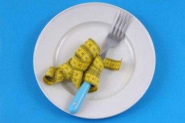 Çatallı diyet kavramı, mavi arka plandaki bir tabakta ölçüm bandıyla çevrili.