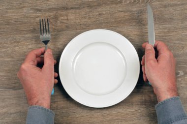 Elinde çatal bıçak takımı olan ve boş tabağı olan biri.