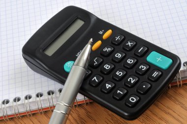 Kalem ve hesap makinesi yakın plan spiral bir defterde.