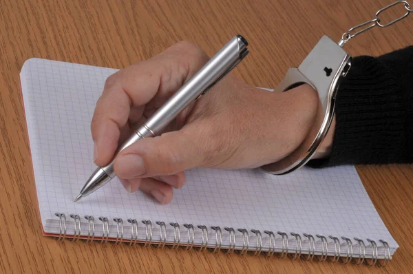 Confession concept with someone handcuffed writing on a spiral notebook with a pen