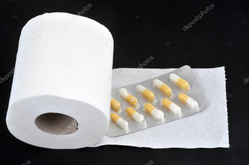 Constipation concept with toilet paper roll and laxative blister pack on black background